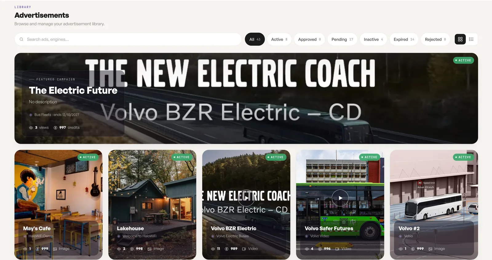 The advertisement library: 43 campaigns as image and video cards with live status, views and credits, a featured bus-fleet campaign pinned on top